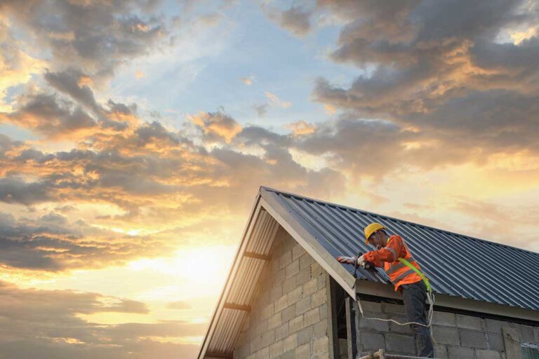 A person on a sturdy ladder attaching holiday lights to the edge of a sloped shingle roof with plastic clips.
