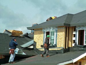 Person inspecting dark water stains and softened plywood roof decking inside a dim attic.