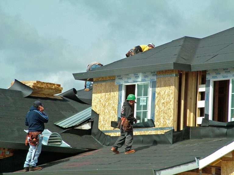 Person inspecting dark water stains and softened plywood roof decking inside a dim attic.