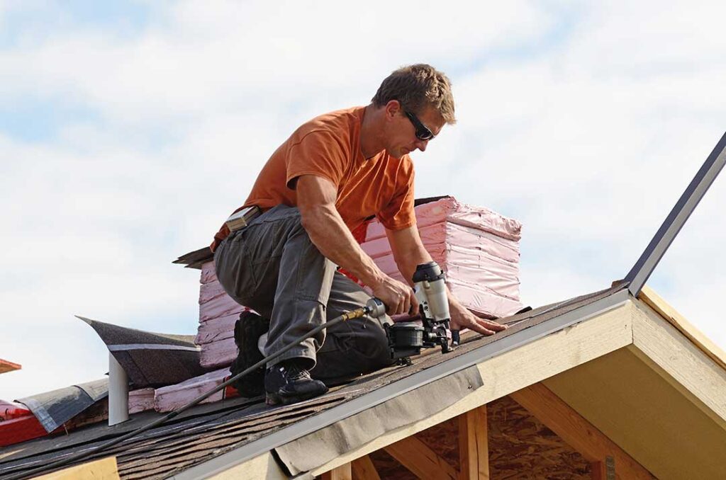 Roof shingles and ridge caps lifted by strong wind beside scattered roofing debris on the ground.